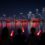 Ilustrasi BTS The City Arirang Singapura: kota tepi teluk menyala merah di malam hari dan siluet fans membawa lightstick