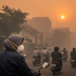 Pengendara motor memakai masker N95 di jalan kota yang diselimuti kabut asap karhutla, ilustrasi cara jaga kesehatan saat kabut asap
