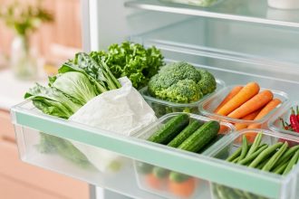 Cara menyimpan sayur agar awet: laci kulkas berisi sayur daun berbungkus tisu, brokoli, wortel, timun, dan buncis dalam wadah kaca